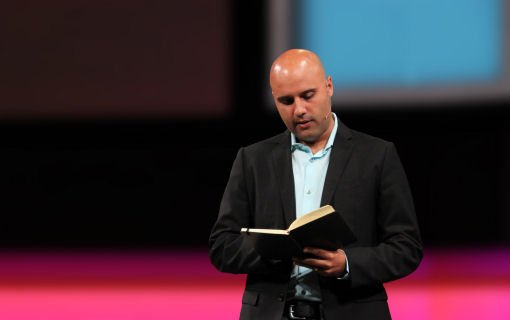 Thumbnail image of Skye Jethani standing on a stage, holding a book