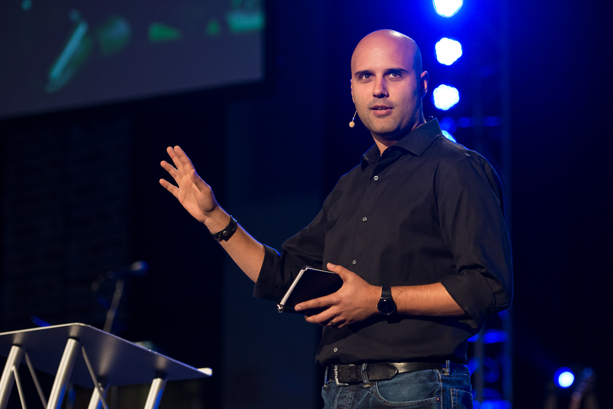 Skye Jethani holding a Bible and preaching behind a pulpit