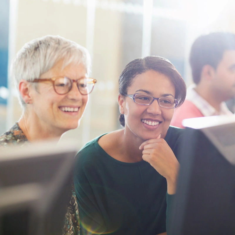 Two women smile while looking at a computer screen