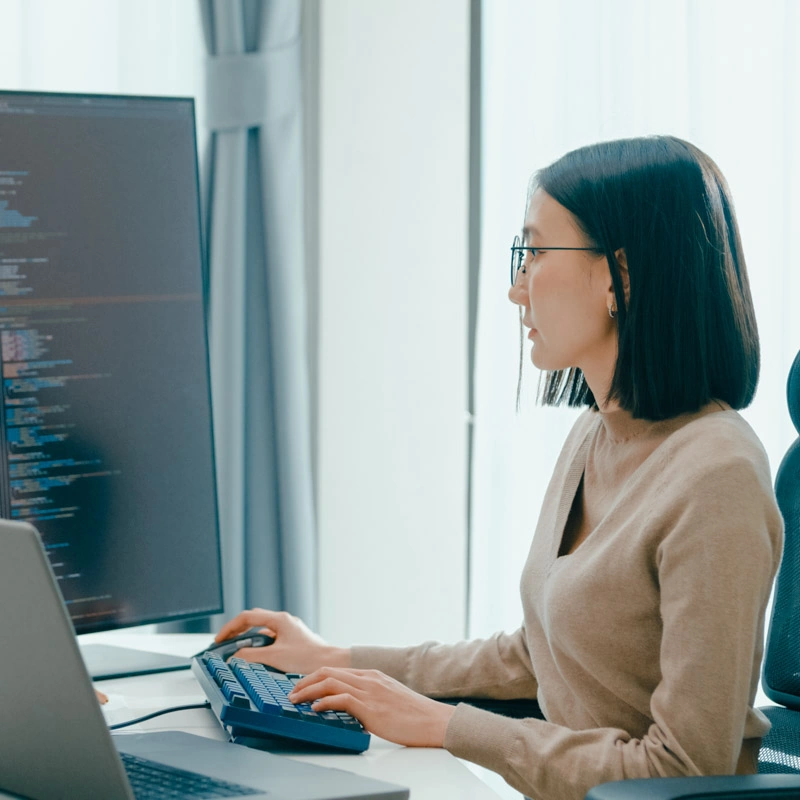 A woman sits and looks at a tall, vertical computer screen
