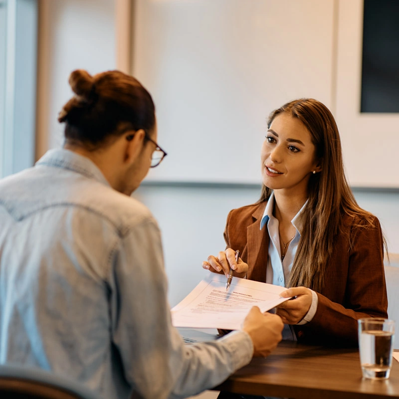 A man and woman sit at a table while the man looks at a paper and the woman looks at the man