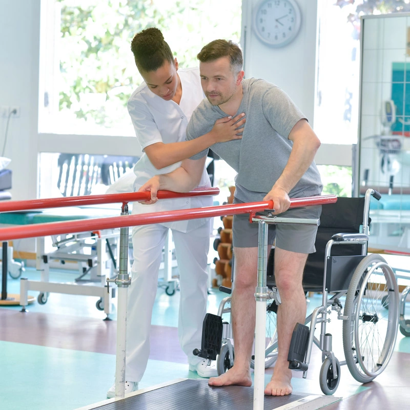 A physical therapist assists a man in walking with arm supports