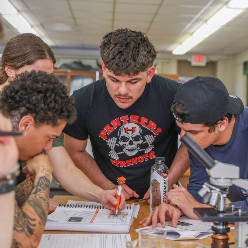 Four students look down at a textbook