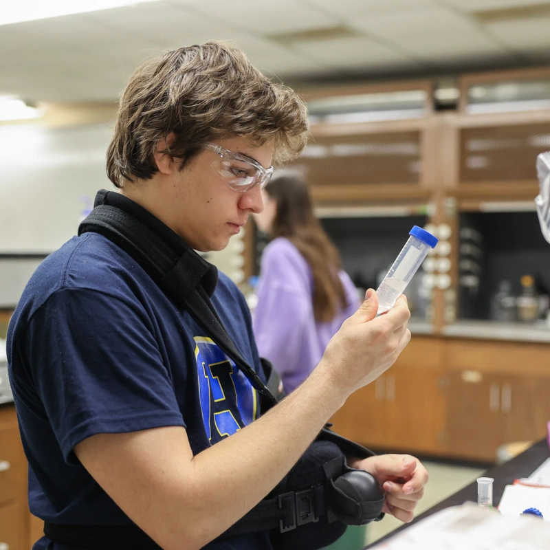 A young white man looks down at a test tube that he is holding