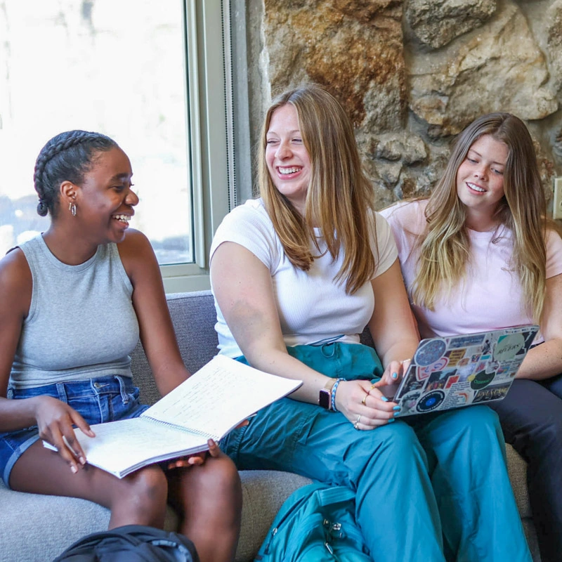 Three young women sit in Gaither Fellowship Hall, smiling