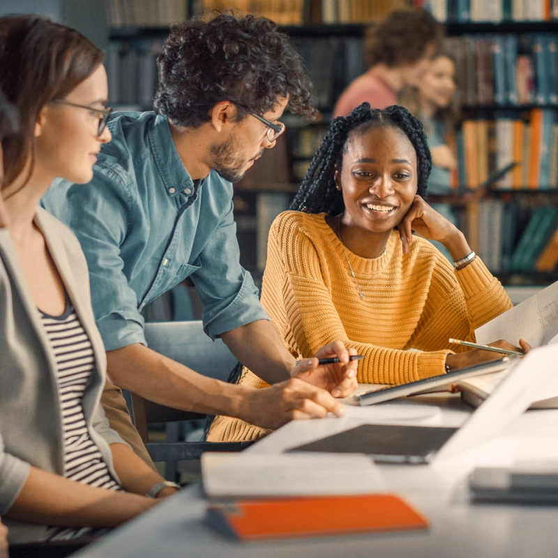 Three students, a young man and two young women, are looking at each other at a table