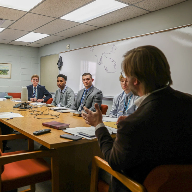 Young men in suits sit around a conference table in the Belk Conference Room