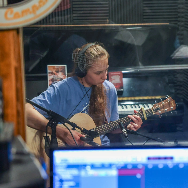 A young woman plays a guitar in a recording studio