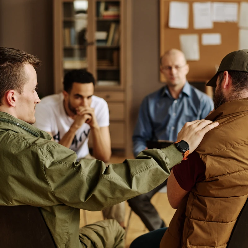 One man places a hand on another's shoulder as men sit in a circle