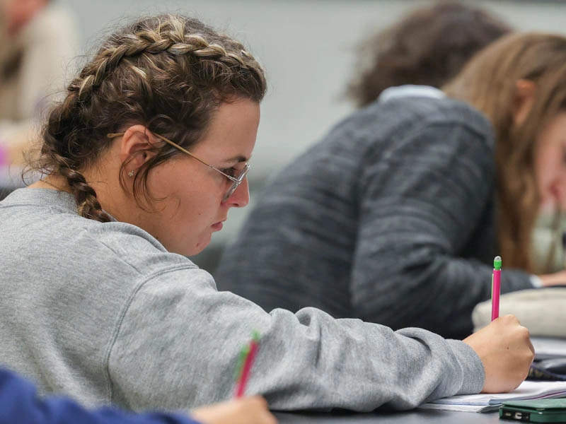 A young woman writes in a notebook with a pink mechanical pencil