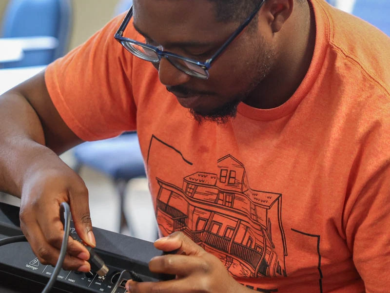 A young man adjusts the cords on an audio mixer