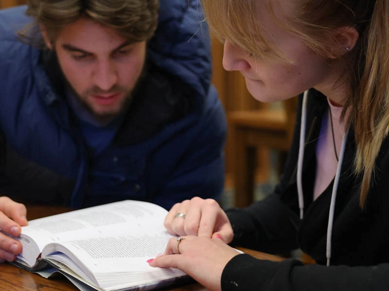 A young man and woman look down at a book