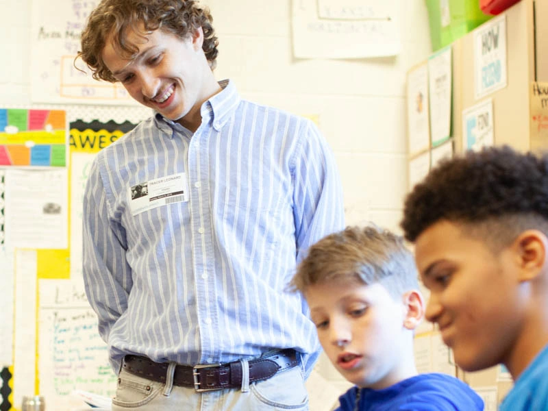 A young man stands and smiles down at two seated boys