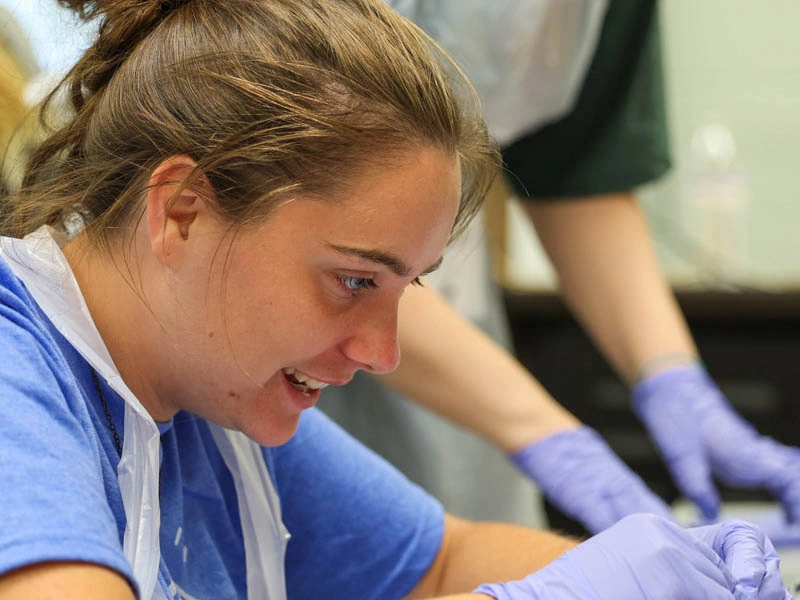A young woman wearing rubber gloves smiles while looking down