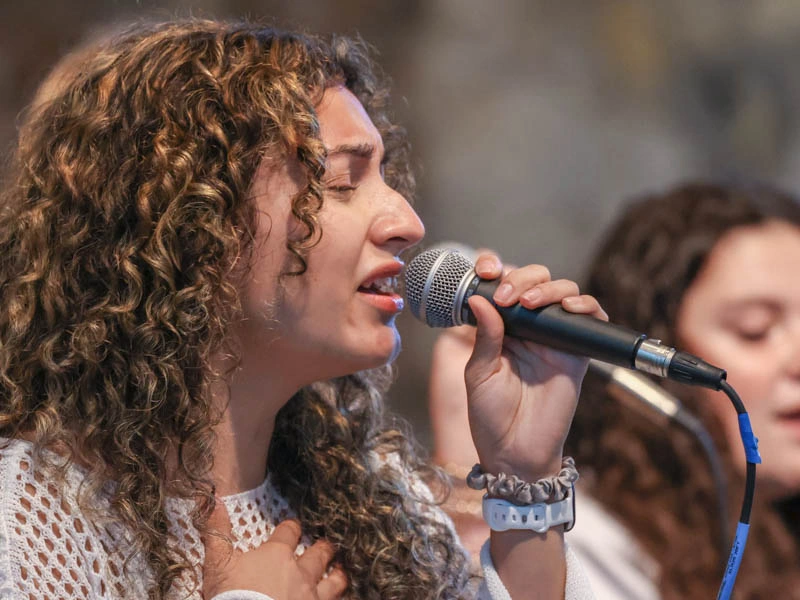 A young woman sings into a microphone with her eyes closed
