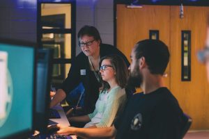 Kelli Burgin stands and talks with two seated students in the Cyber Lab