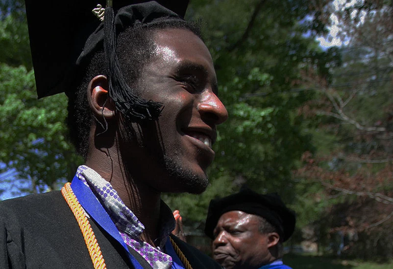 Young man smiles while wearing commencement cap and gown