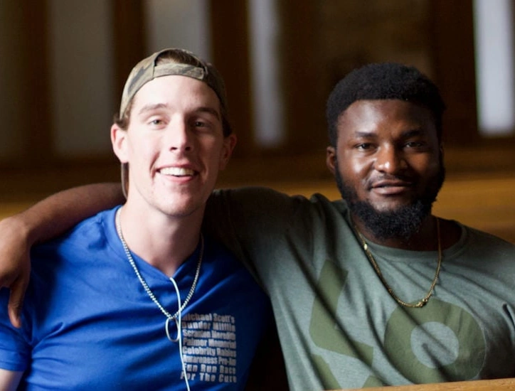 Two young men sit with arms around each others' shoulders