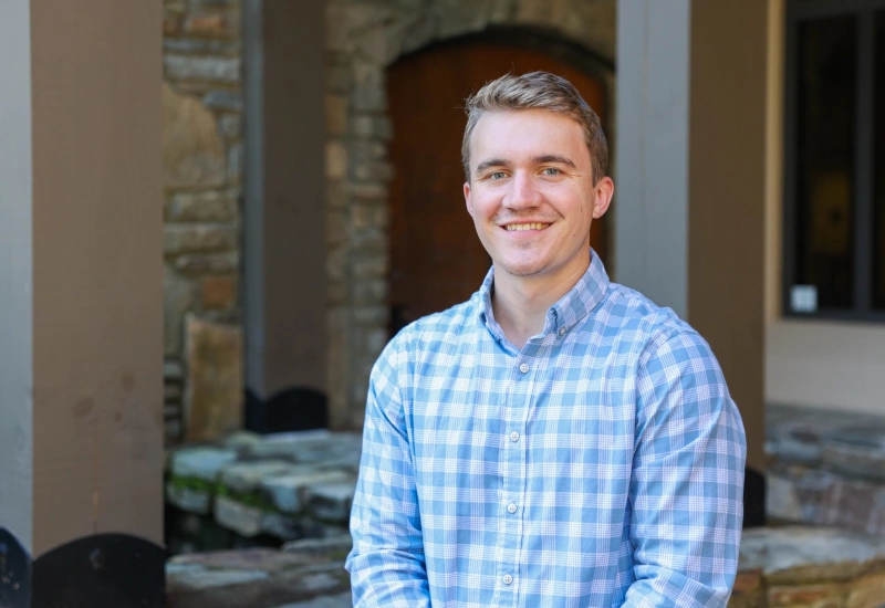 A young man wearing a plaid shirt smiles