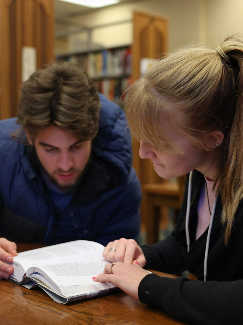 A young man and woman look down at a Bible