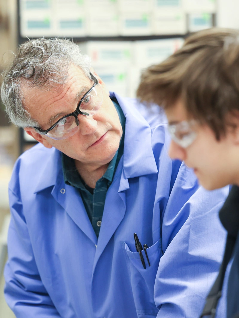 A professor in a lab coat looks at a young male student