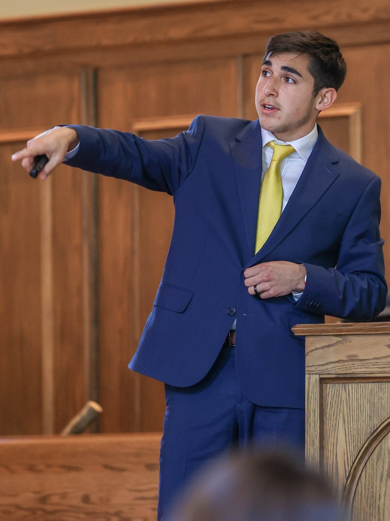 A young man in a suit speaks from a podium