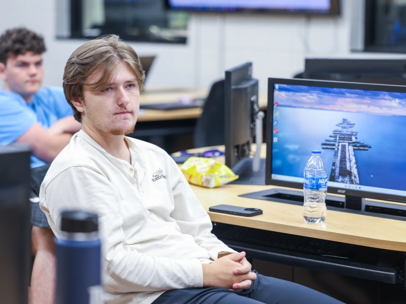 A young man sits in front of a computer screen