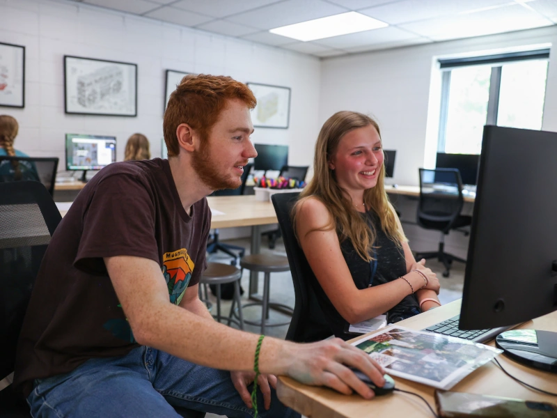 A young man and woman look at a computer screen