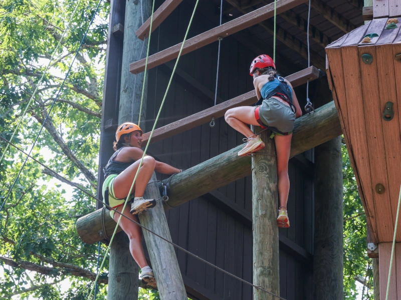 Two women climb a high ropes course