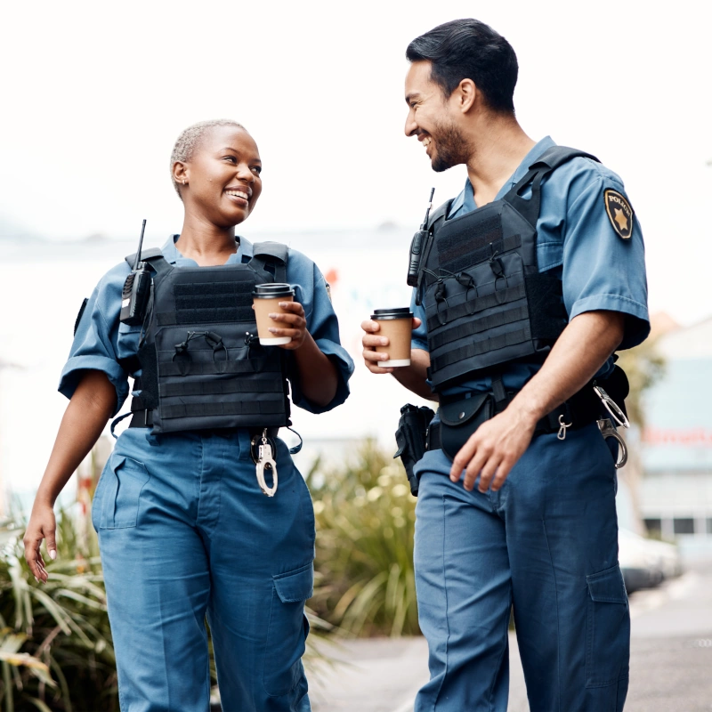 Two police officers in bulletproof vests smile broadly while looking at each other