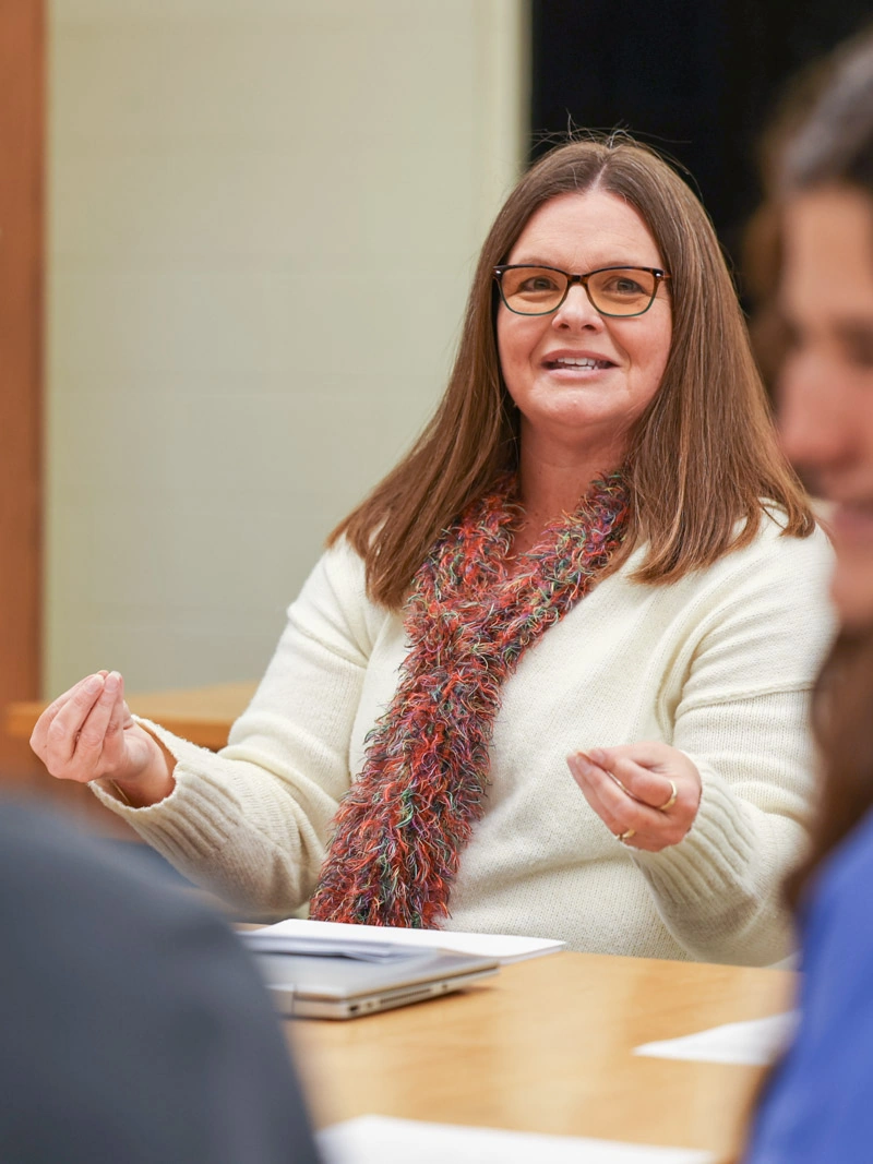 A middle-aged woman smiles and gestures with both hands
