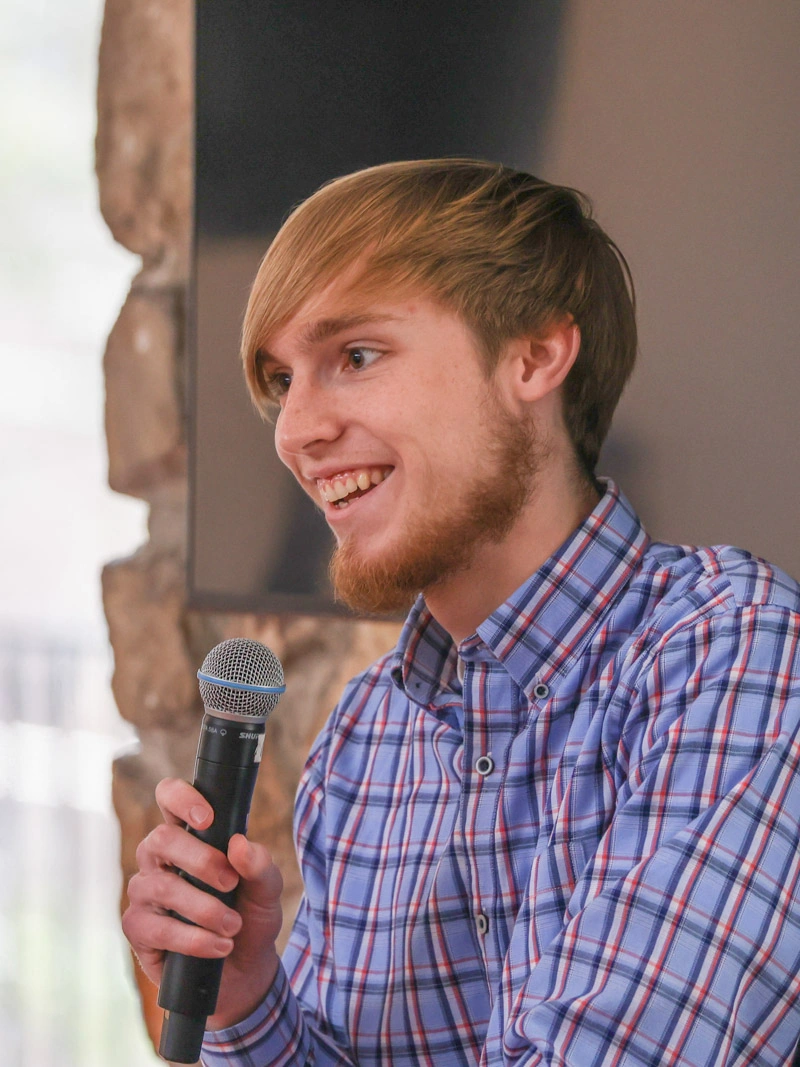 A young man smiles widely while holding a microphone