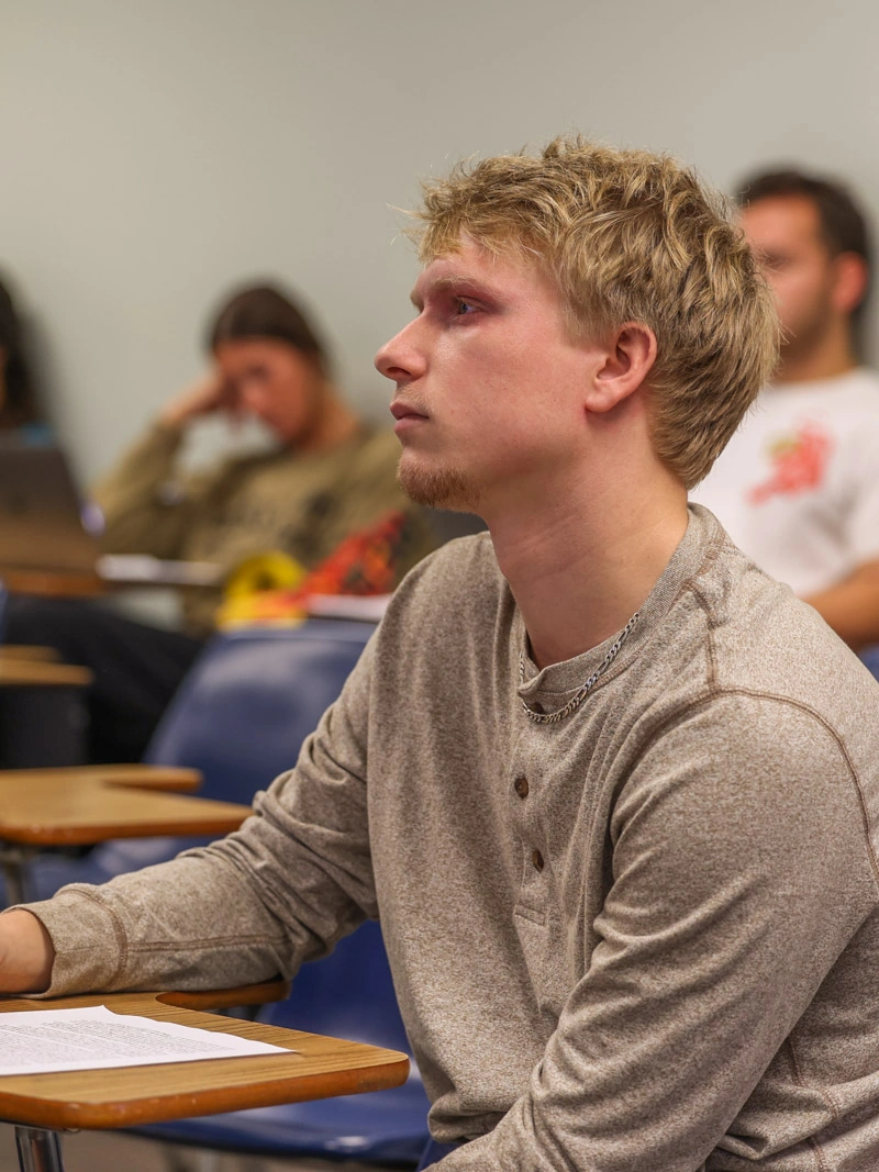 A young man sits at a desk and looks forward