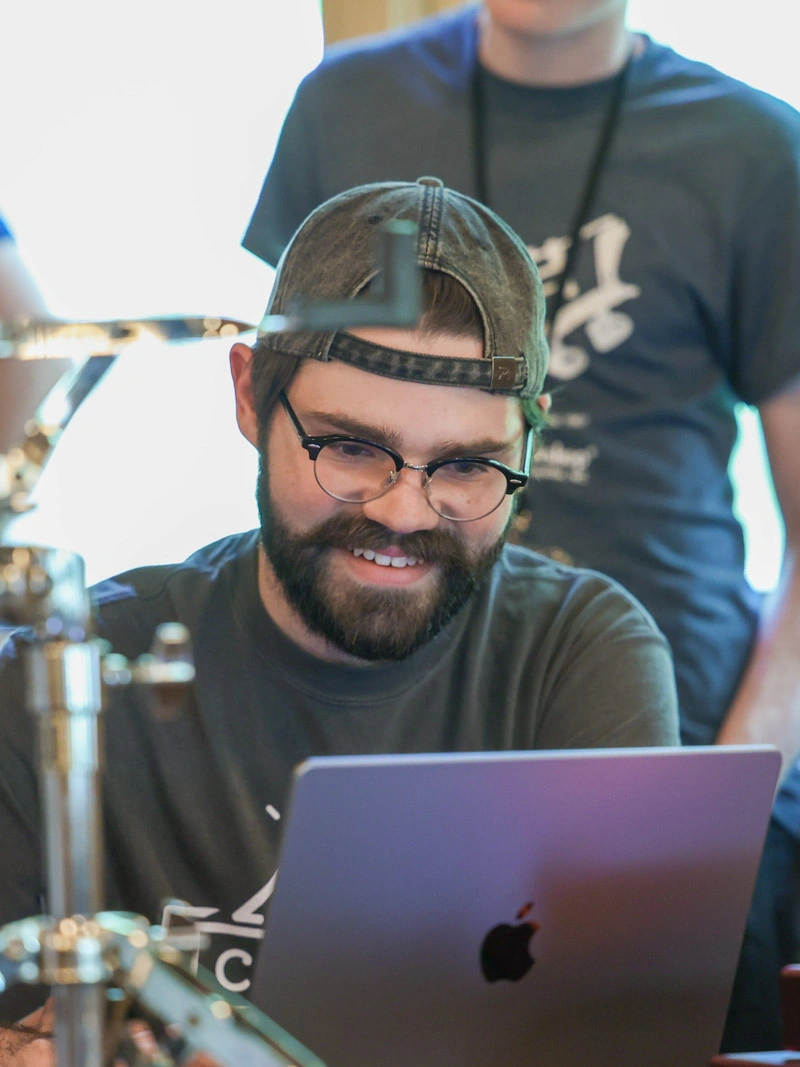 A young man smiles while looking at a Mac laptop