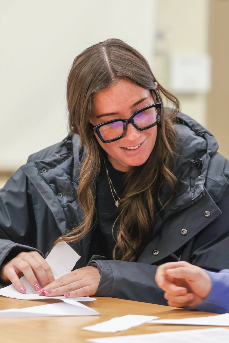 A smiling woman wearing a black jacket looks down at the table