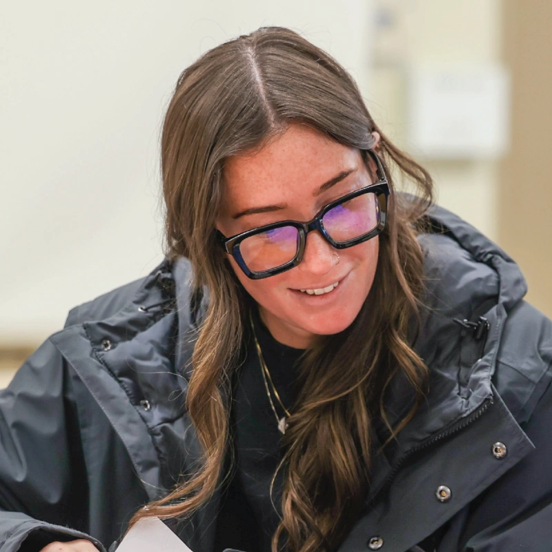 A smiling woman wearing a black jacket looks down at the table